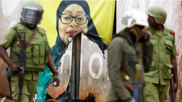 A file image of police walking past a vandalized campaign poster in Tanzania.